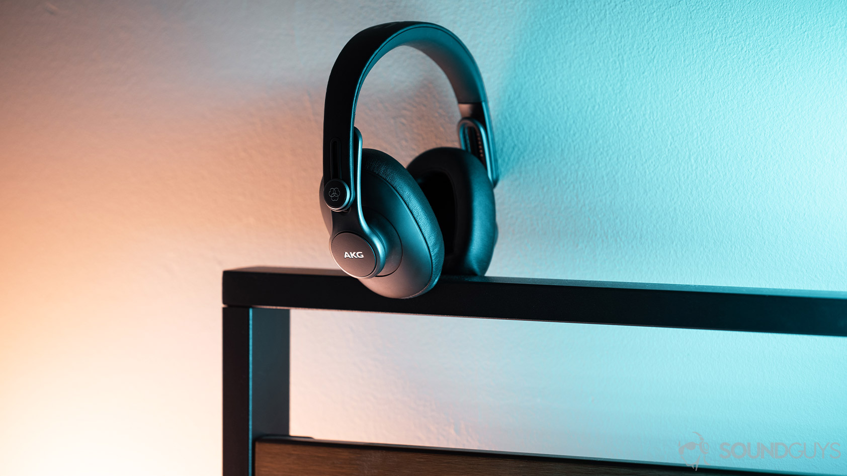 The AKG K371 wired over-ear headphones on an iron bedrame lit by blue and orange lights.