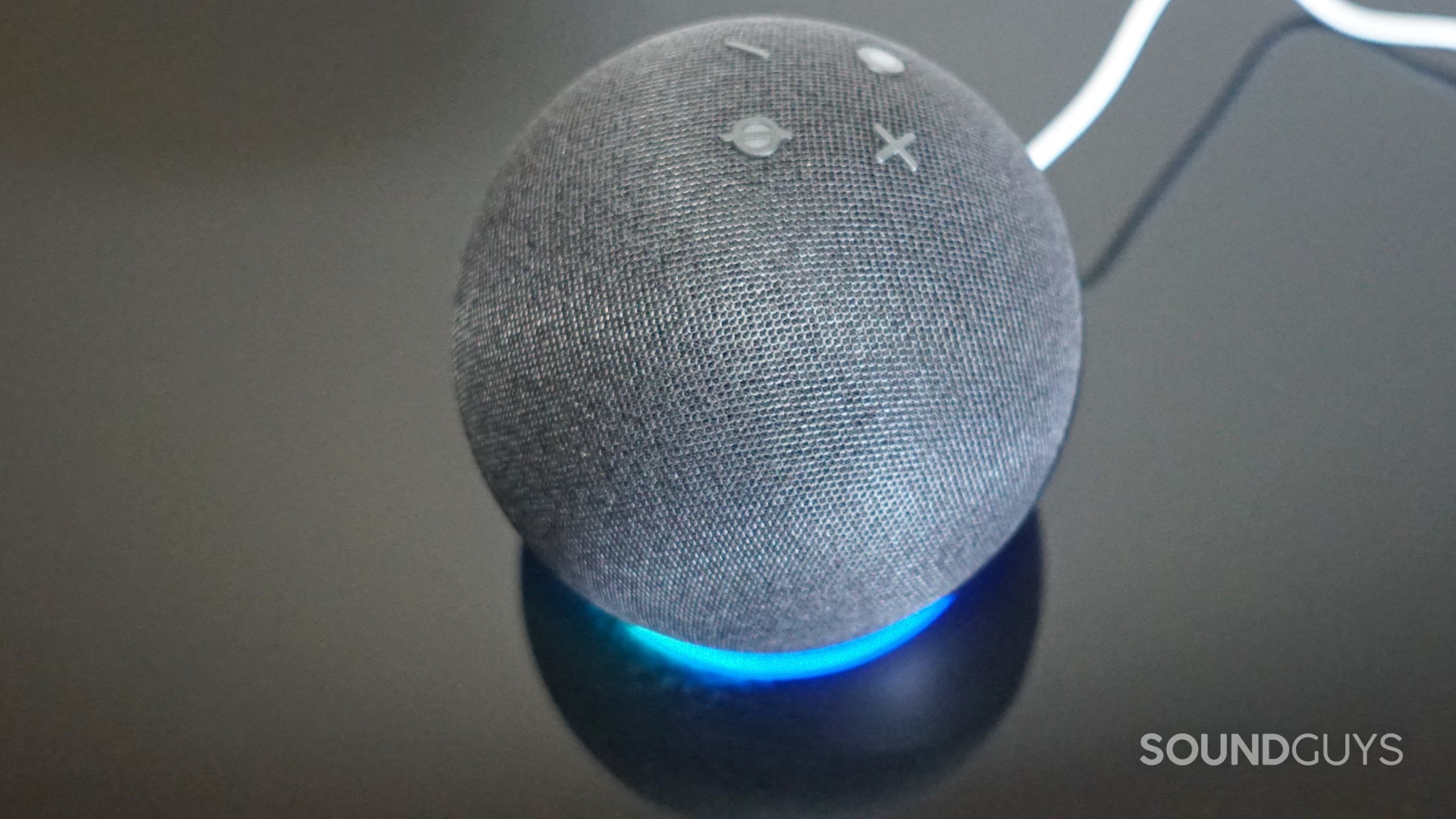 The Amazon Echo Dot (5th Gen) sits on a reflective black surface with its LED light turned.
