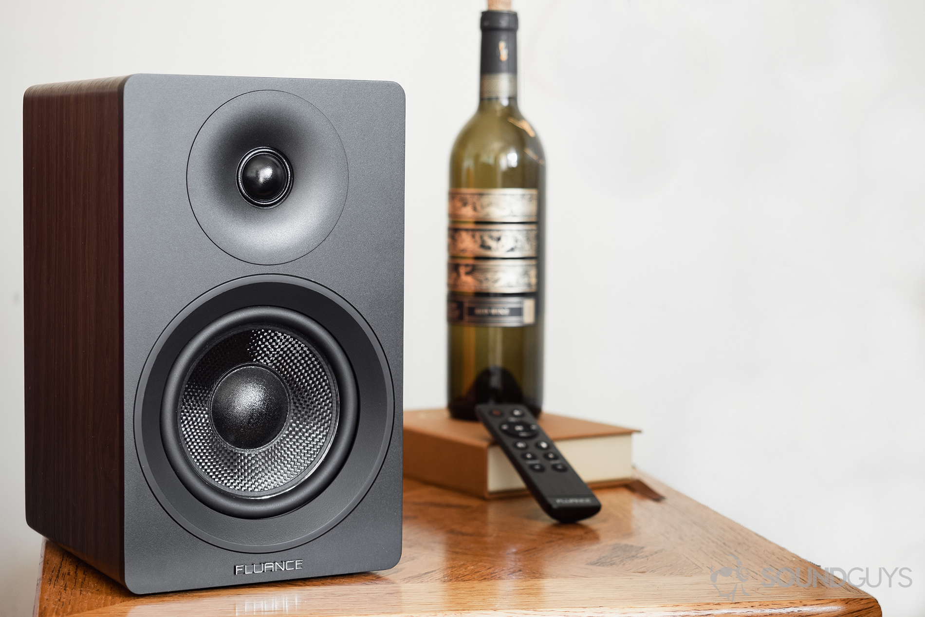 Fluance Ai40 review: The passive speaker on a table with a wine bottle in the background and the remote.