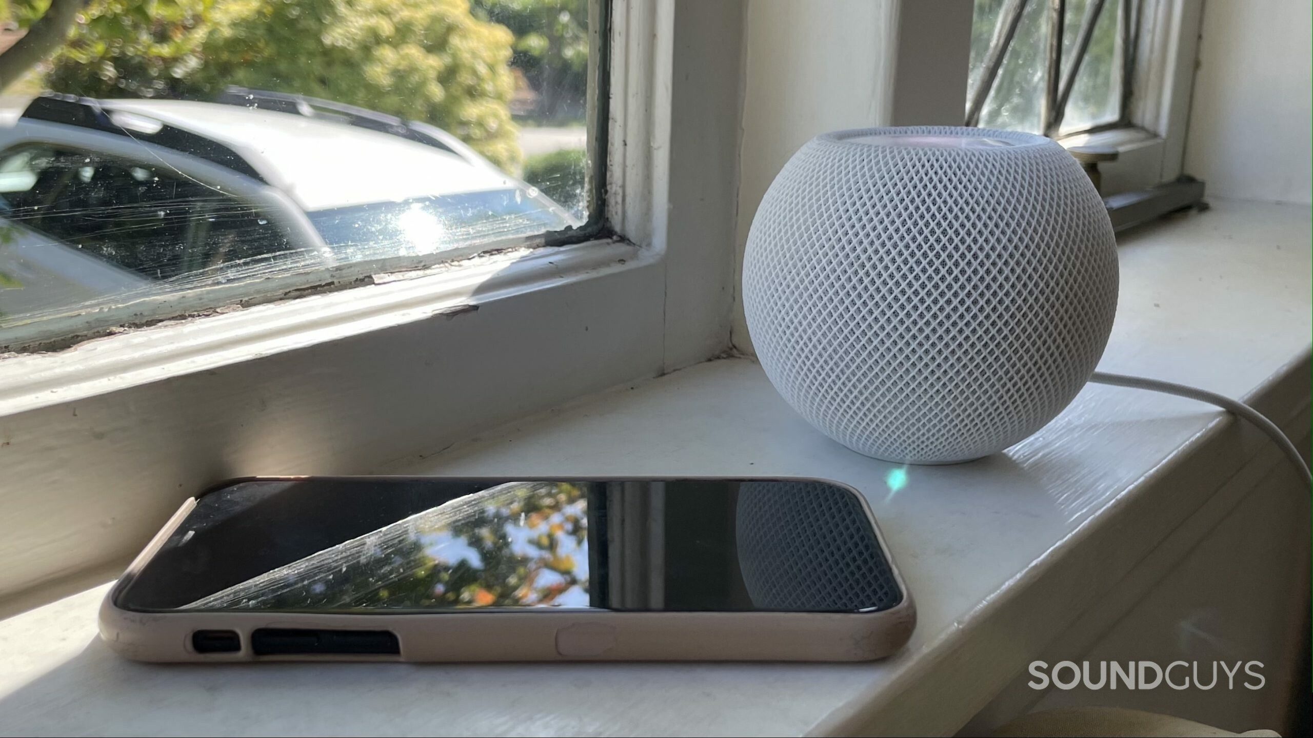 An iPhone and Apple HomePod mini on a windowsill.
