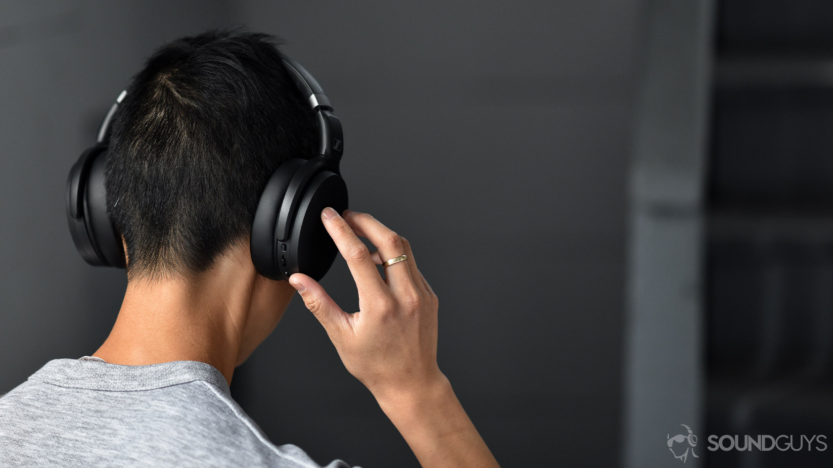 The Sennheiser HD 450BT noise canceling headphones worn by a woman as she adjusts the volume via the onboard controls on the right ear cup.