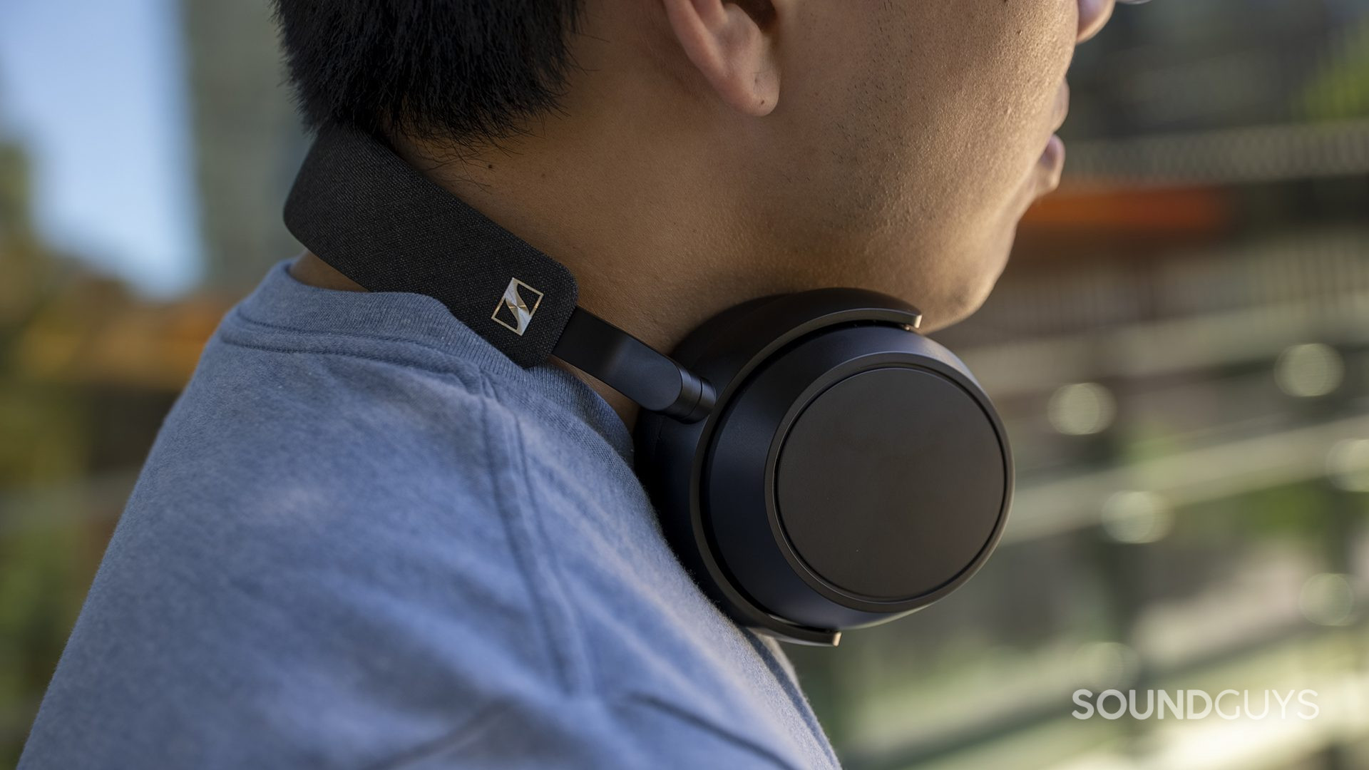 A man wears the Sennheiser MOMENTUM 4 Wireless around his neck while outside.