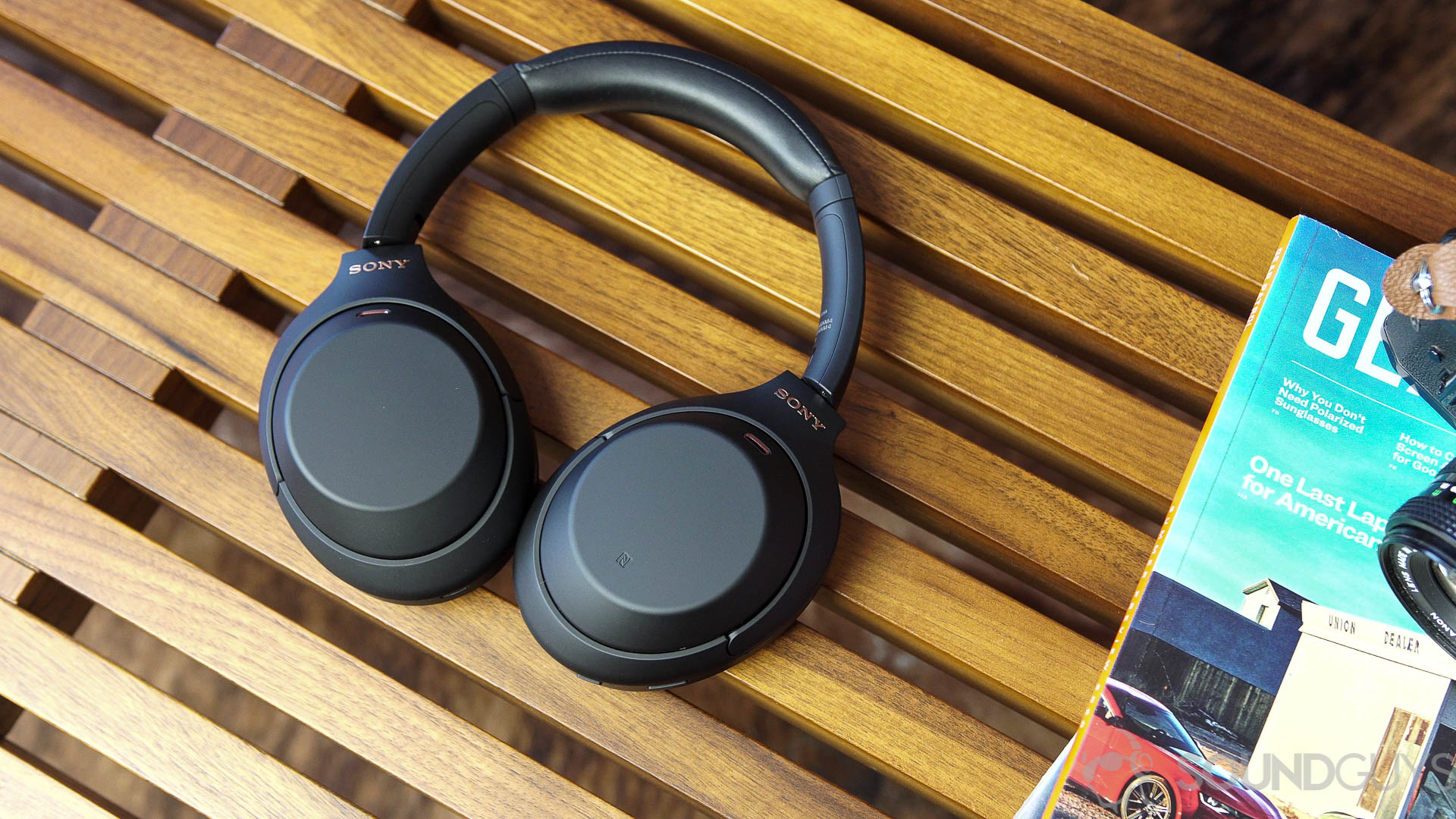 Sony WH-1000XM4 headphones next to magazines on a wood bench